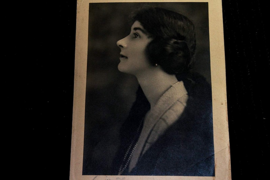 A black and white photo taken side on of a woman with her hair in a side bun wearing a fur coat