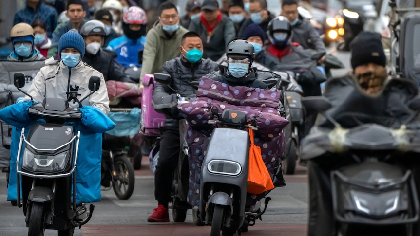 Traffic on motorbikes, riders wear face masks. 