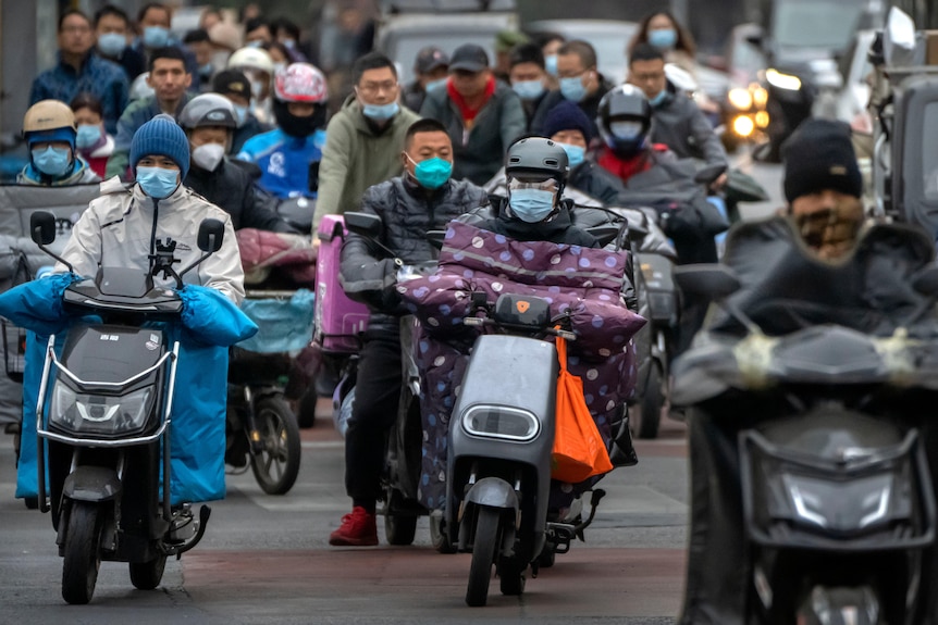 Traffic on motorbikes, riders wear face masks. 