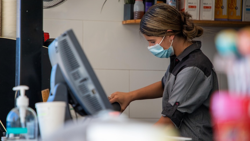 A side-on shot of a barista wearing a face mask while making a coffee.