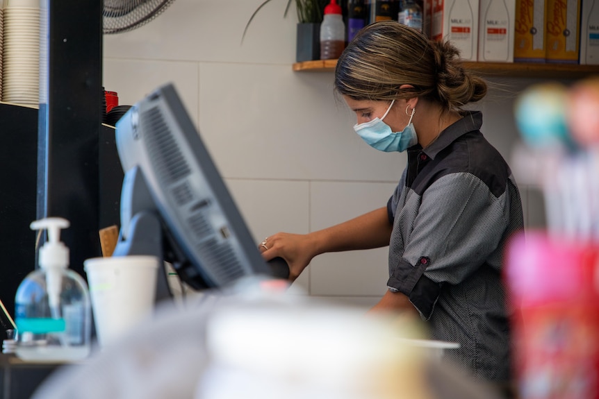 A side-on shot of a barista wearing a face mask while making a coffee.