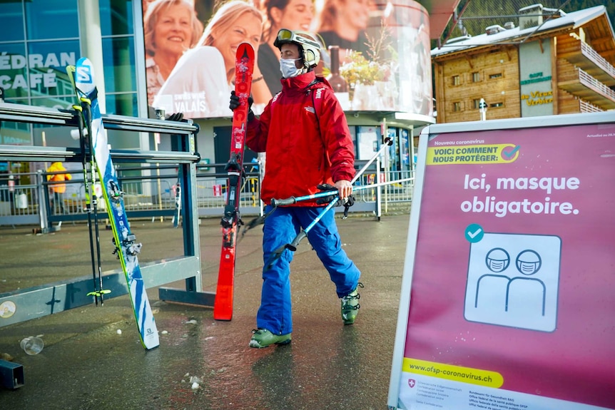 A skier walks past a sign in French with a face mask on it