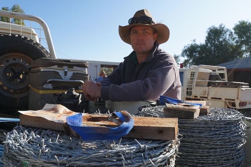 A man standing behind a ute with a tray full of rolls of barbed wire.