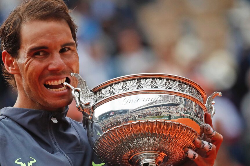 Rafael Nadal holds his French Open trophy and pretends to bite one of its handles
