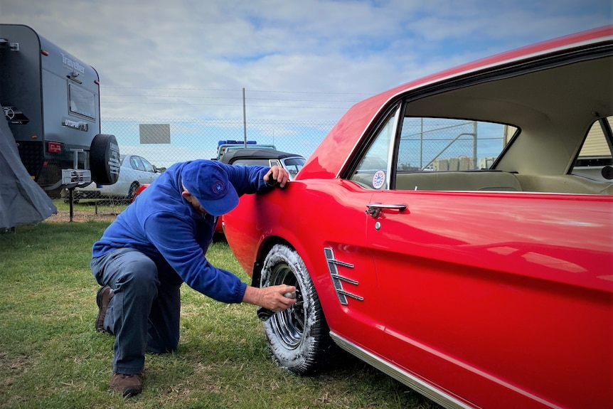 A man washing the tyres of his shiny, red, vintage car.