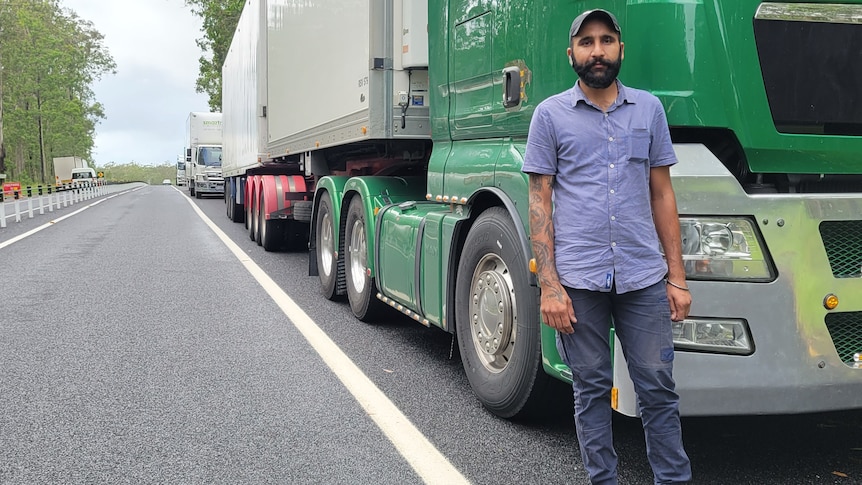 A man stands in front of his big rig, which is just one in a long line of trucks.