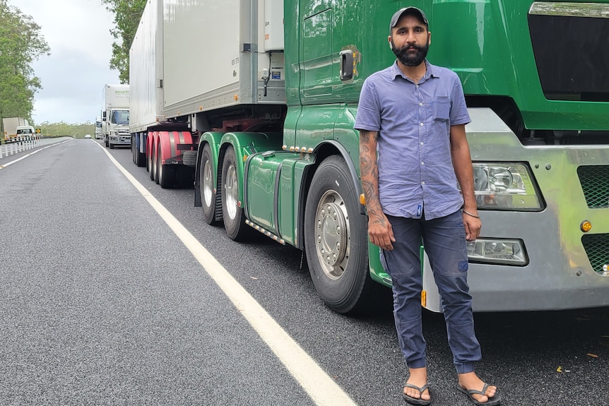 A truck driver stands on the road in front of his rig.