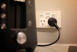 A black toaster is plugged into a white electricity socket, with two plugs and a third switch labelled "fridge".