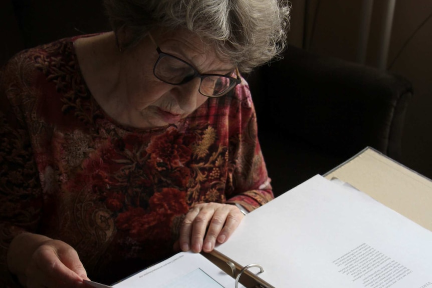 Salomea Genin reads a page in a large binder, several pages are flagged with post-it notes.