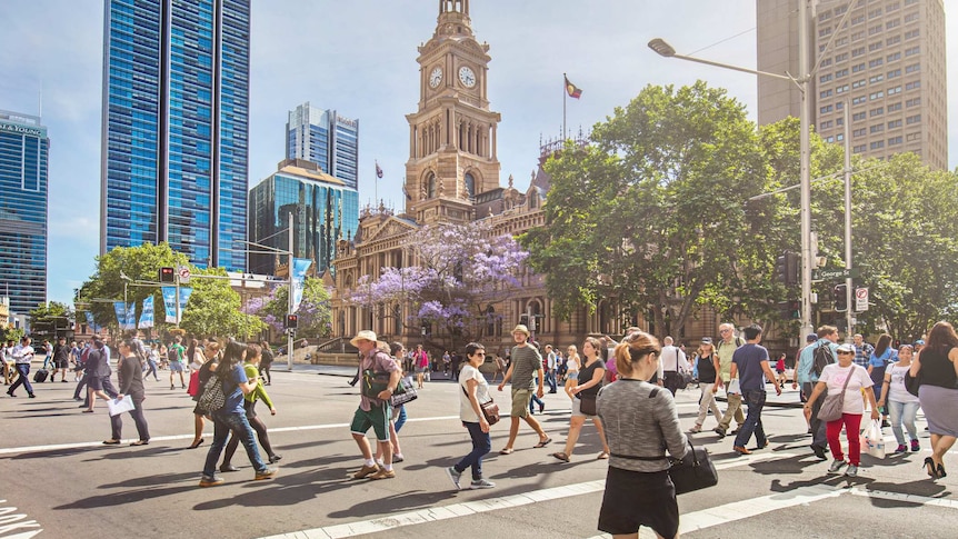 People cross the busy intersection at Sydney Town Hall on a bright, sunny day.