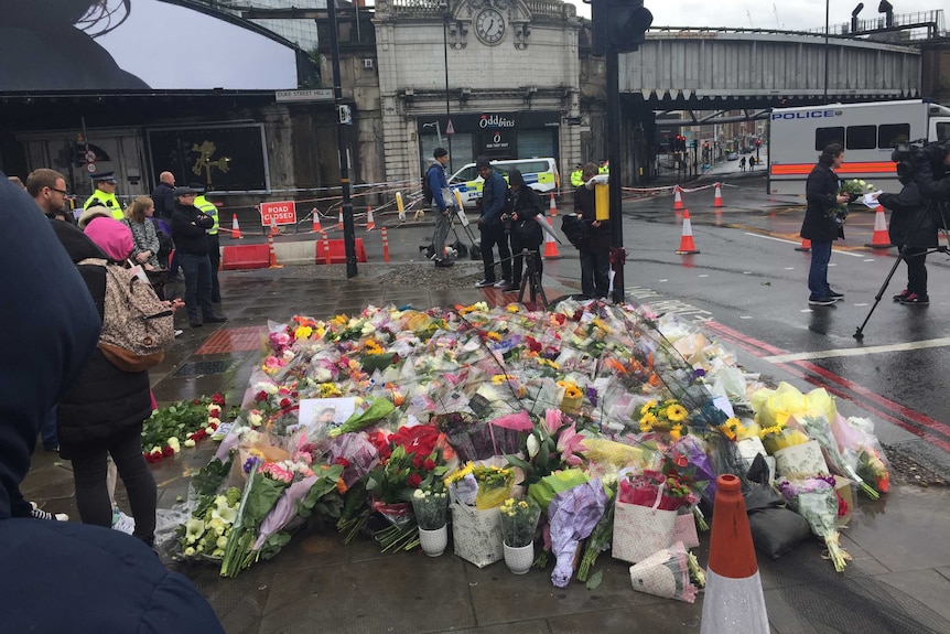 A large collection of flowers sit by the side of the road on a rainy day in London.