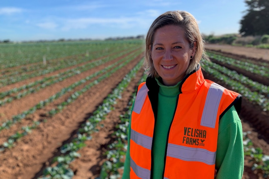 A woman in a vest labelled "Velisha Farms" stands amongst crops.