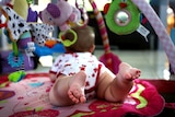 A baby plays under a mobile.