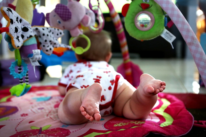 A baby plays under a mobile.