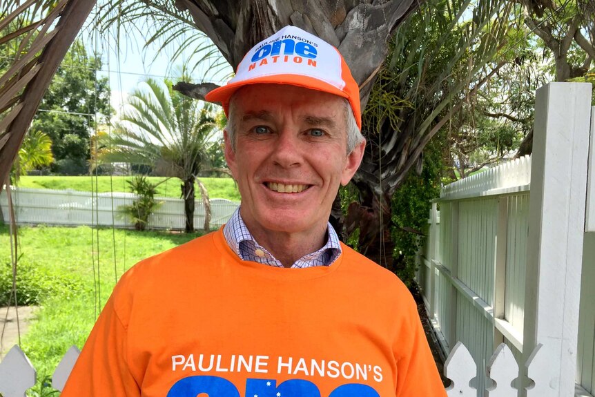 Malcolm Roberts smiles while wearing a One Nation t-shirt and cap