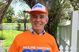 Malcolm Roberts smiles while wearing a One Nation t-shirt and cap