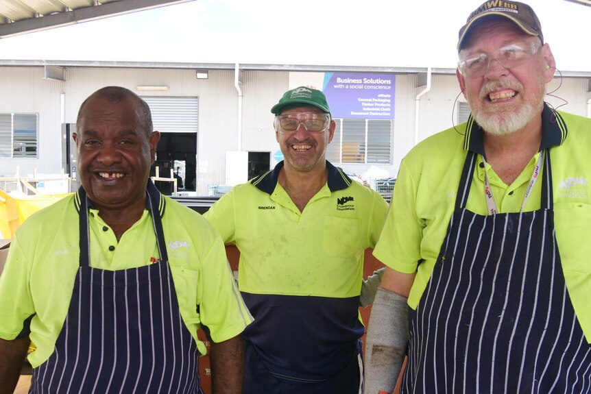 three men in fluro yellow shirts and aprons stand together.