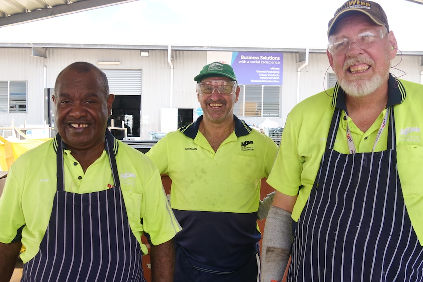 three men in fluro yellow shirts and aprons stand together.