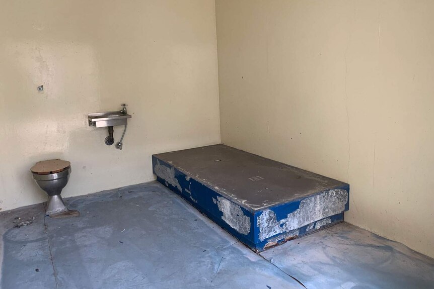 Inside an old cell at the closed Boggo Road jail in Brisbane showing concrete bed, floor, stainless steel toilet and handbasin.