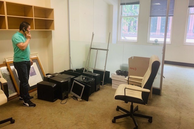 Man talks on a phone with furniture and desktop computers on the floor next to him.