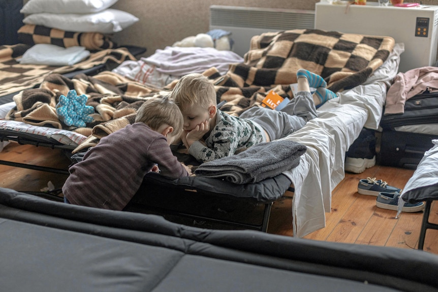 Dwoje małych dzieci w pokoju z zestawem przenośnych łóżek polowych.