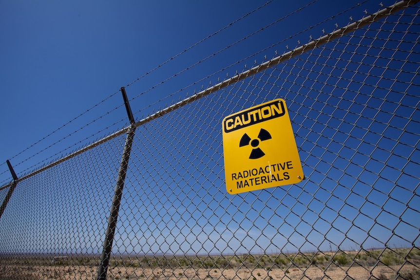 An image of a radioactive warning sign on a fence against a clear sky