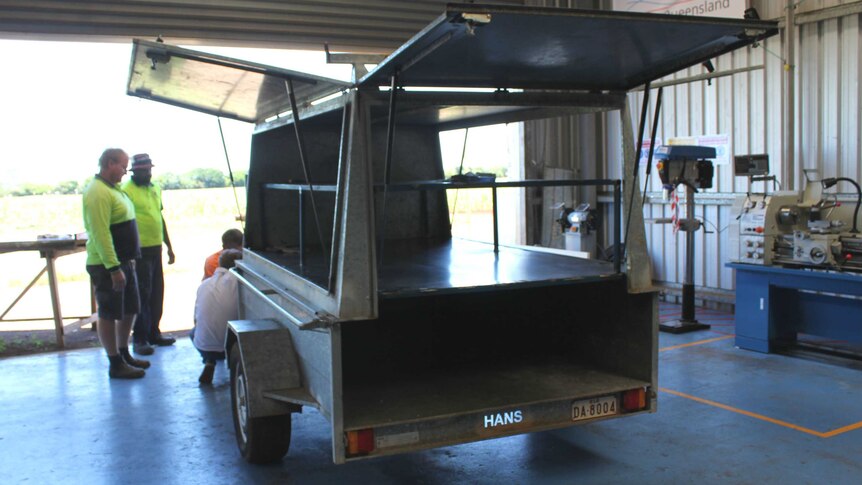 An aluminium trailer is being modified by a group of men in a workshop