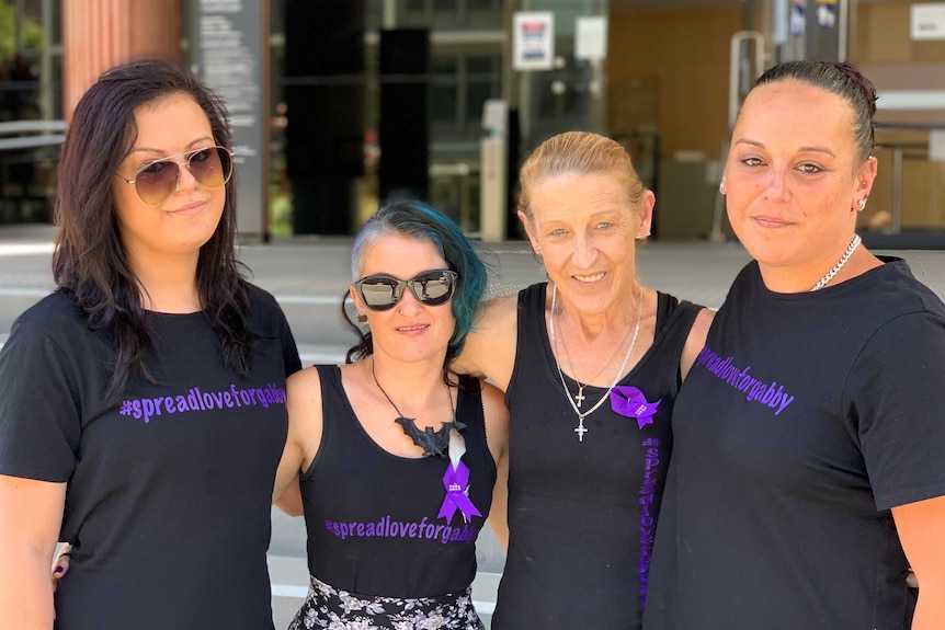 Four women with their arms around each other outside a court house.