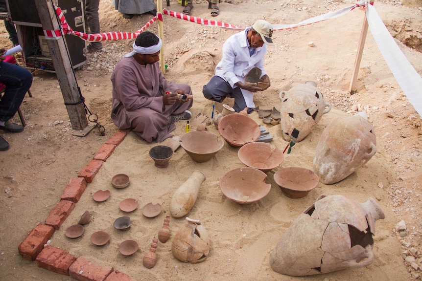 Men clean and assess broken plates and clay pots