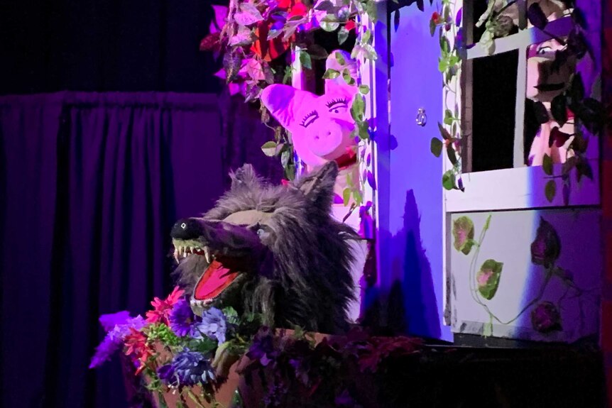Three little pigs and a wolf on stage during a puppet performance