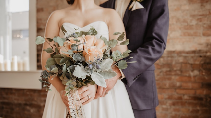 Bride holding flowers, and groom, faces obscured.