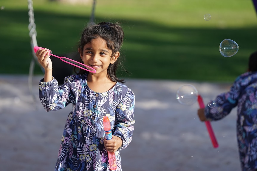 A little girl smiles while holding a pink bubble wand