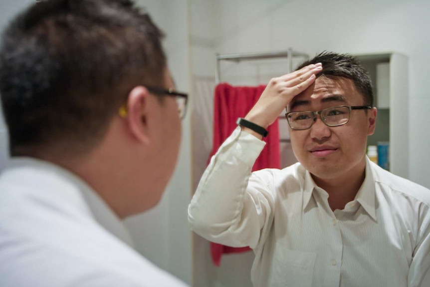 A young man is fixing his hair in the mirror as he gets ready to go out