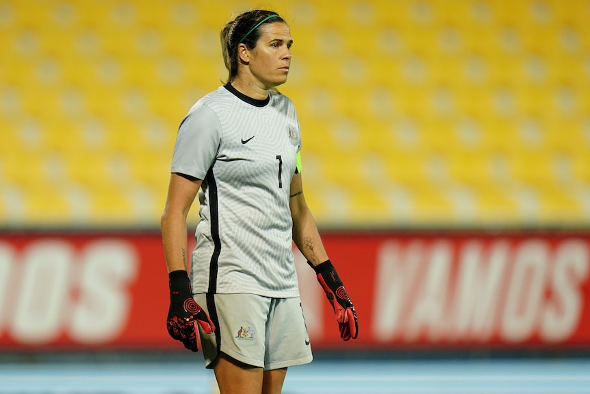 A woman in a grey soccer uniform and gloves