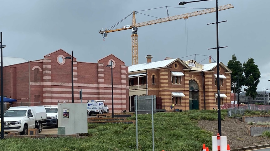 Two yellow and red brick buildings stand beside each other with a crane in the backgound and construction at the front