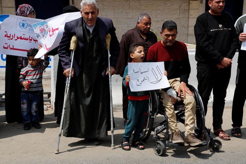 Palestinian children and elderly in crutches and protest outside a UN office in Gaza.