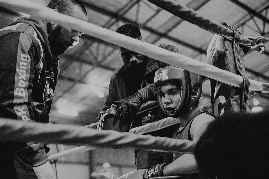 Wearing protective head gear, Kael Burns sits in the corner of the ring during training at Derrick's Boxing