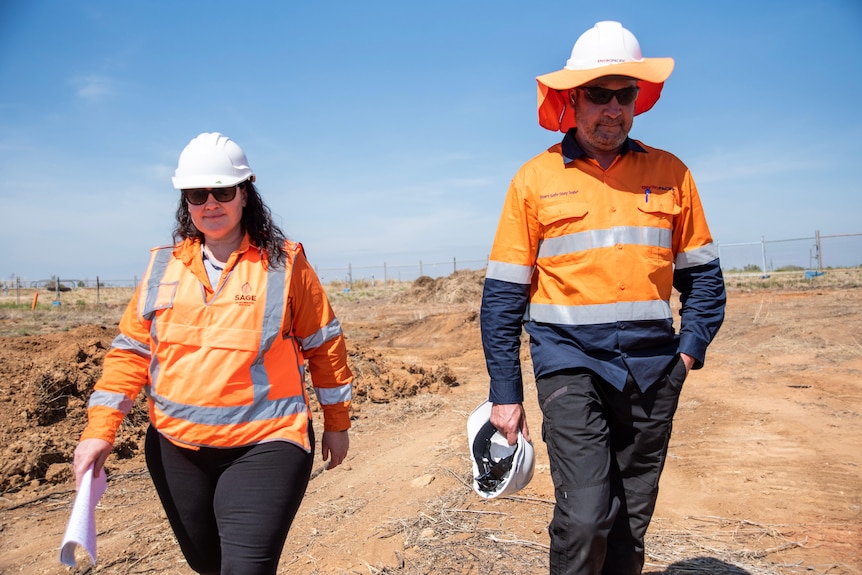 A woman and a man in high-vis walk side by side through a dusty plot of land.