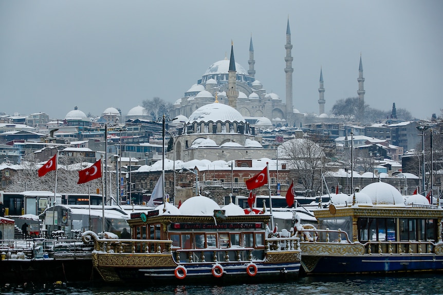 Tourist boats docked in front of a mosque covered in snow in Istanbul