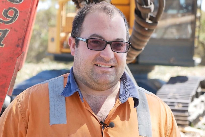 Brendon Penny stands in front of a harvesting machine.