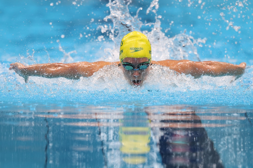 A woman swimming in a yellow swimming cap raising her arms above the water