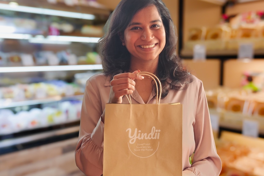 Woman smiling holding a brown paper bag with branding 'Yindii'.