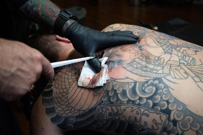 Man can be seen tattooing a man using the tebori method onto a man's back