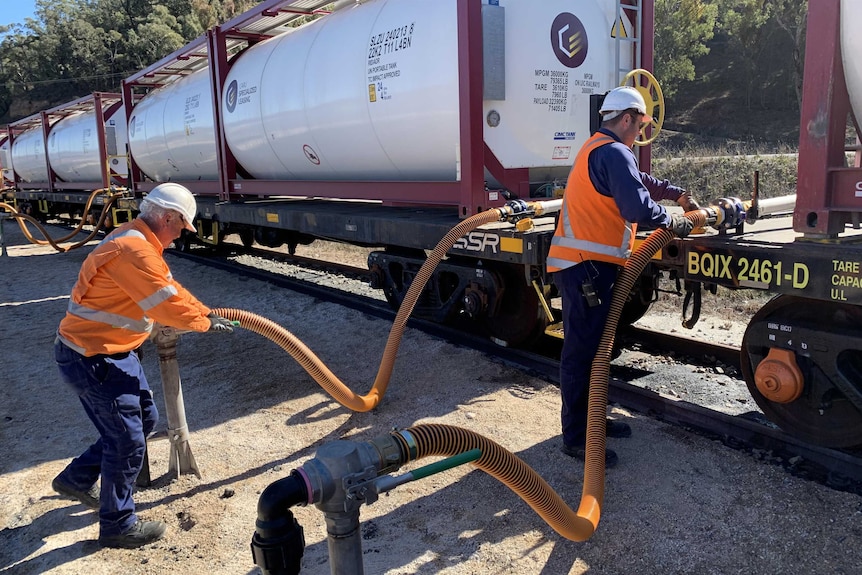 Two crew members attach hoses at Charbon's loading station to the tankers.