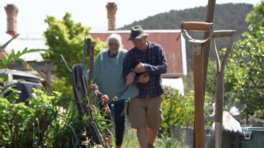 Man leading elderly lady through a home garden