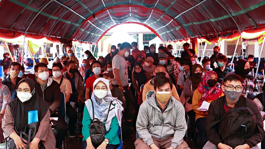 People wearing protective face masks sit before receiving a dose of the coronavirus disease (COVID-19).