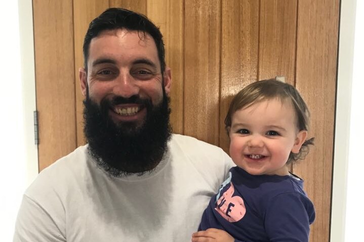 man in white top and long dark beard holding toddler smiling