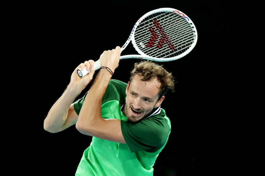 Male tennis player, wearing a green shirt, follows through with a shot during a night match