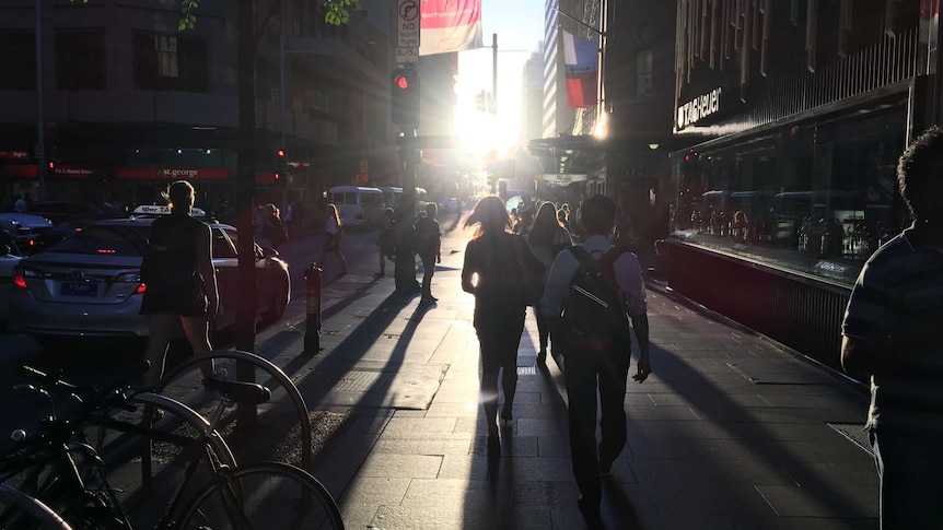 Shoppers walk up Market Street in the Sydney CBD into a bright sunset.