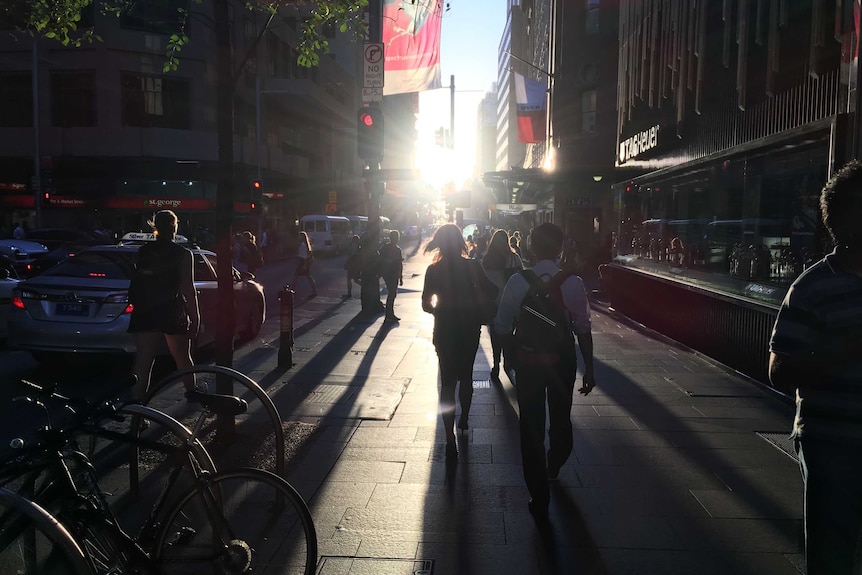 Shoppers walk up Market Street in the Sydney CBD into a bright sunset.